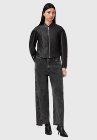 Giubbotto cropped in pelle nera con chiusura a zip e spalle strutturate, abbinato a jeans grigi a vita alta e gambali larghi, con stivaletti neri.