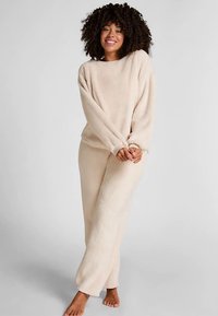 Beige, zachte lounge set met een loszittend shirt met lange mouwen en bijpassende broek met elastische boorden, ontworpen voor comfort en warmte.