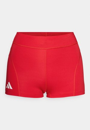 Red athletic shorts made from smooth fabric. Features a high waistband and stitching details. Includes a white logo on the lower left.