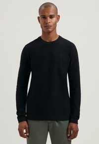 Fekete, hosszú ujjú crew neck pulóver strukturált anyagból, bordás mandzsettákkal és diszkrét logóval a mellrészen. Világos színű nadrágokkal kombinálható.