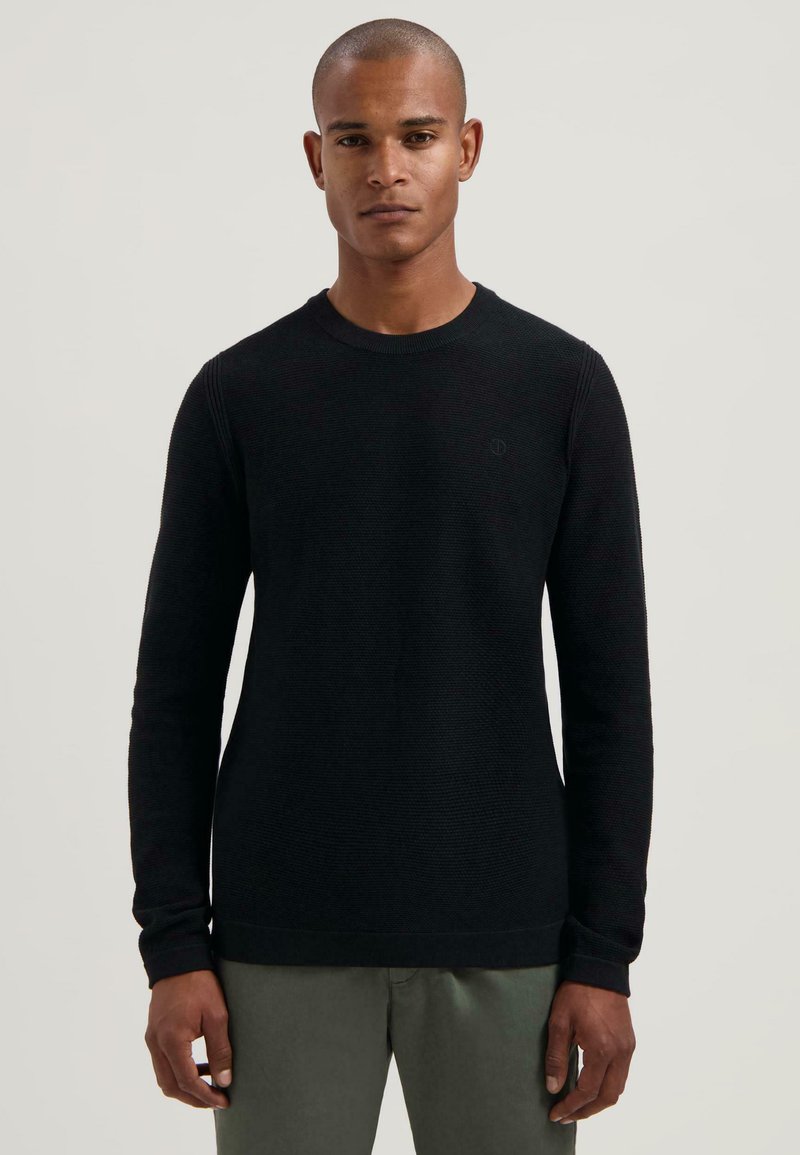 Fekete, hosszú ujjú crew neck pulóver strukturált anyagból, bordás mandzsettákkal és diszkrét logóval a mellrészen. Világos színű nadrágokkal kombinálható.