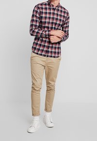 Camicia a quadri in blu navy, rosso e bianco; abbinata a chinos beige e sneaker bianche. Presenta maniche lunghe e colletto classico.