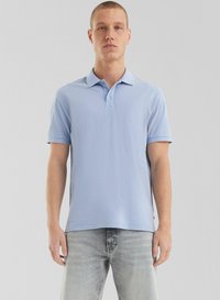 Polo shirt bleu clair avec une patte de boutonnage à trois boutons, manches courtes et texture douce ; associé à un jean gris clair.