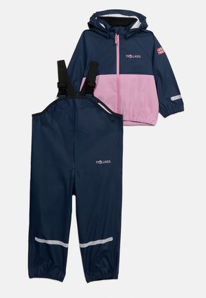 Detská nepremokavá bunda v námorníckej modrej a ružovej farbe s kapucňou a zodpovedajúce nepremokavé námornícke nohavice s nastaviteľnými čiernymi trakmi a reflexnými pásikmi.
