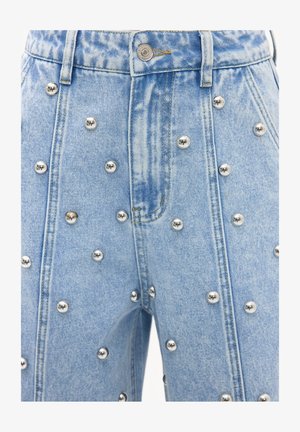 Vaqueros de mezclilla azul claro con cintura alta, decorados con tachuelas metálicas plateadas distribuidas de manera uniforme en los paneles frontales.