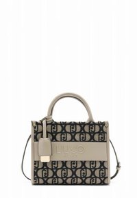 Beige handbag with a textured fabric featuring a dark emblem pattern, top handles, detachable shoulder strap, and a logo-accented panel.