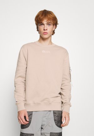 Beige sweatshirt with long sleeves and crew neck, featuring a white logo on the chest and a zip pocket on the left sleeve.