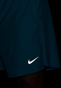Calções desportivos Nike em tecido verde-azulado escuro com textura suave. Apresentam um logótipo swoosh branco no lado inferior esquerdo.