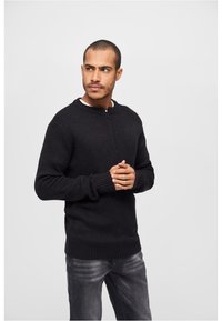 Jersey negro de punto con cuello alto y media cremallera, con puños y dobladillo acanalados. Combinado con jeans gris oscuro.
