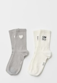 Coppia di calzini con una paio grigio con design a cuore e una paio bianco con il testo "SOHO", entrambi in tessuto a maglia a coste.