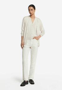 Ljusrosa cardigan över en V-ringad topp, beige byxor och svarta loafers. Cardiganen har knappstängning och ribbade muddar.