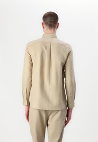 Beige hosszú ujjú ing klasszikus gallérral, gombos mandzsettával és hátsó redőzéssel. Könnyű anyagból készült.