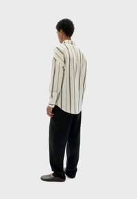 Camisa de manga larga a rayas en color crema y negro con cuello, combinada con pantalones negros sueltos y zapatos grises sin cordones. Textura de tela suave.