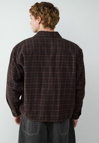 Braun karierter Langarmhemd mit entspannter Passform, weicher Textur, knöpfbaren Manschetten und Kragen. Die Rückseite verfügt über eine Passe und sichtbare Nähte.