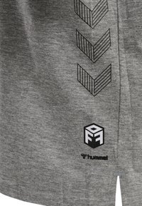 Grå jersey tyg med svarta grafiska chevron-mönster och en logotyp vid fållen. Texturen är mjuk med en avslappnad design.