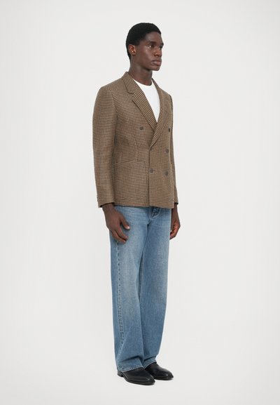 Brun houndstooth dubbelknäppt blazers med slag, matchad med ljusblå vida jeans och svarta skor. Enkel vit t-shirt under.