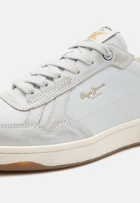 Baskets gris clair avec une tige en cuir lisse, des accents texturés, un bout rond et des lacets plats. Logo doré "Pepe Jeans" sur le côté.