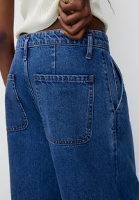 Blå denimjeans med hög midja, två bakfickor och kontrasterande sömmar. Tyget har en lätt struktur och en klassisk passform.