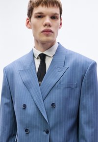 Sacou bleumarin cu dungi albe verticale, cu două rânduri de nasturi, rever decupat și nasturi închiși la culoare. Dispune de un buzunar pe piept.