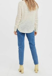 Pull en tricot crème à coupe décontractée, avec un motif texturé, associé à un jean en denim bleu et des chaussures à talons bloc beiges.