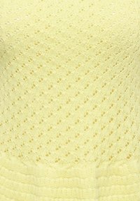 Tissu tricoté jaune avec un motif de dentelle en losange répétitif et une bordure côtelée en bas.