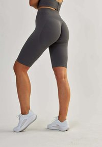 Grijze high-waisted fietsshorts met geribbelde textuur en een contourerende pasvorm, gecombineerd met witte sportschoenen met subtiele mesh-accenten.