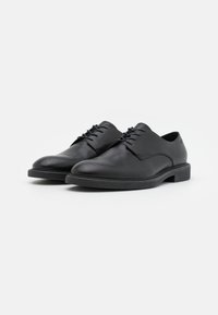 Scarpe in pelle nera con punta rotonda, lacci piatti e un design minimalista. Presentano una superficie liscia e una suola in gomma a profilo basso.