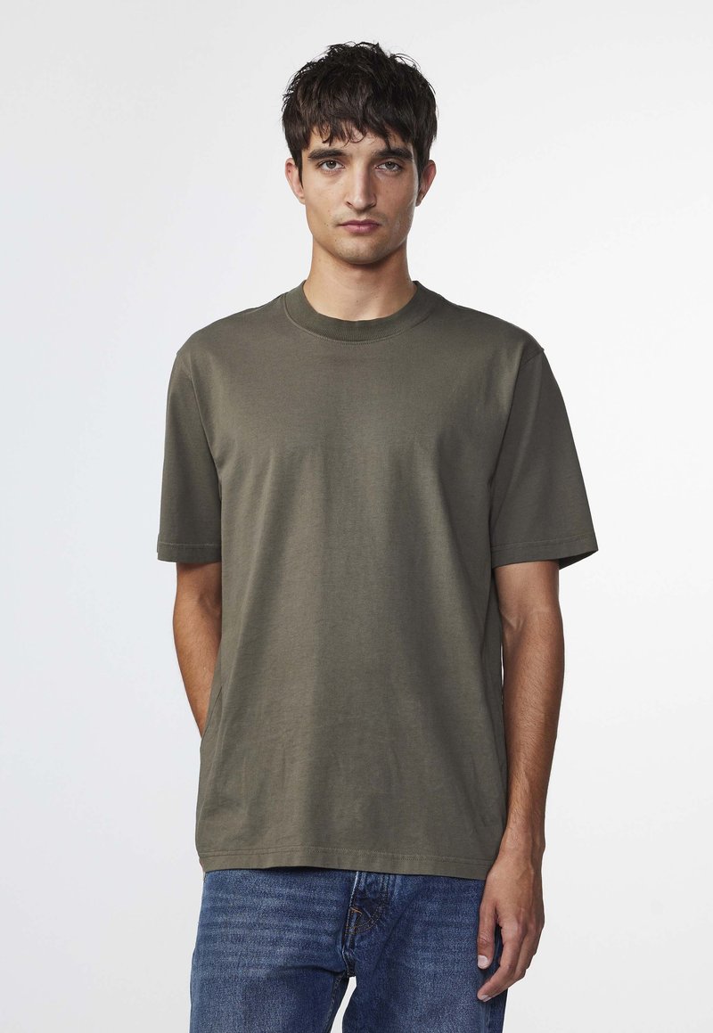 Olivengrøn kortærmet t-shirt med rund halsudskæring, lavet af blødt bomuldsstof. Kombineret med blå denim jeans. Enkel design, ingen mønstre.