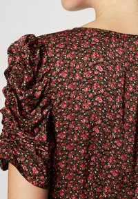 Robe noire à fleurs avec manches bouffantes froncées. Présente de petites fleurs roses et rouges sur un fond sombre, mettant en valeur la texture du tissu.