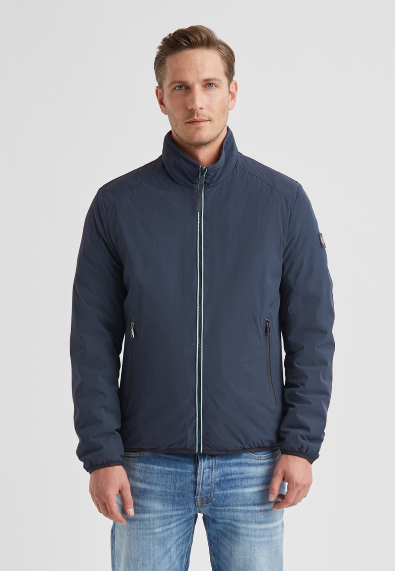 Marineblaue Jacke mit Reißverschluss, hohem Kragen und zwei seitlichen Taschen. Verfügt über einen kontrastierenden hellblauen Reißverschluss und ausgeprägte Schulternahtnähte.