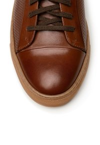 Brązowe skórzane sneakersy z perforowanymi bokami, ciemnobrązowymi sznurowadłami, zaokrąglonym noskiem i teksturowaną gumową podeszwą z kontrastującą jasnobrązową krawędzią.
