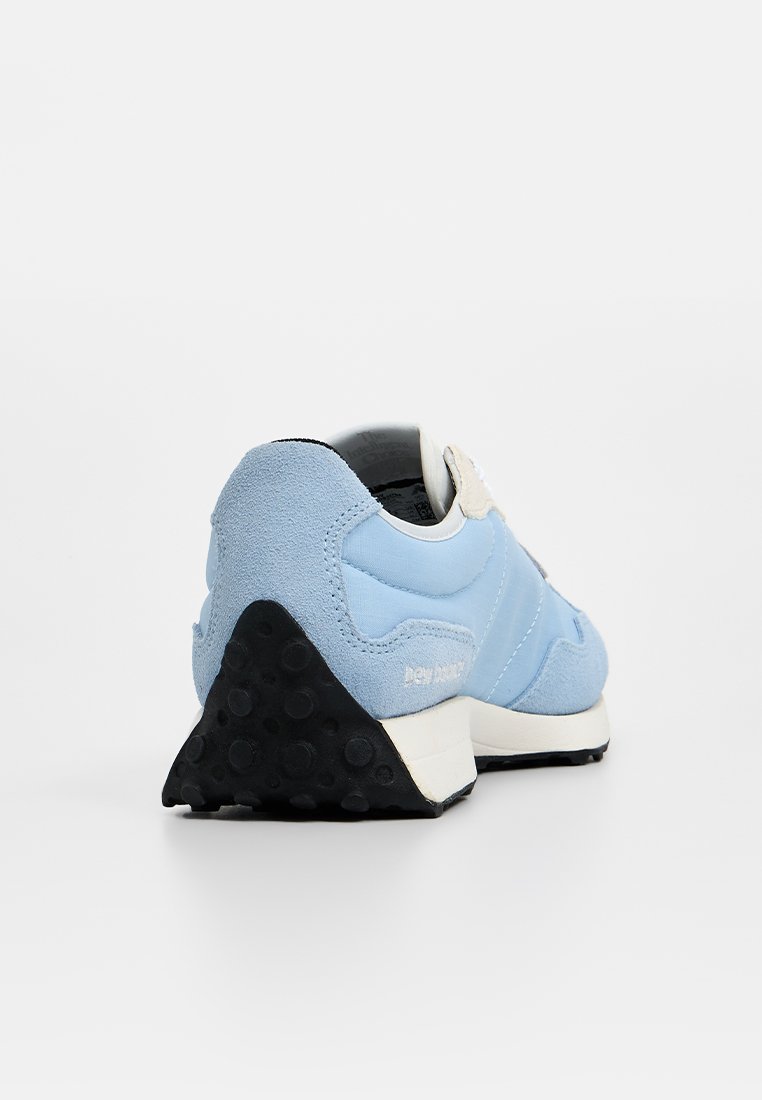 Zapatilla azul con parte superior de ante y textil, una forma distintiva en el talón trasero y una suela de goma negra con patrones de tracción circulares.
