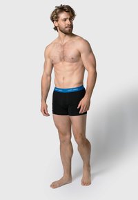 Zwarte katoenen boxershorts met een blauwe elastische tailleband, met de merknaam "HAPPY SHORTS" aan de voorkant. Model met een lichte huid en kort haar.
