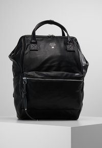 Mochila de cuero negro con asas dobles, bolsillo frontal con cremallera, textura suave, detalle del logo en la parte frontal y una silueta estructurada.