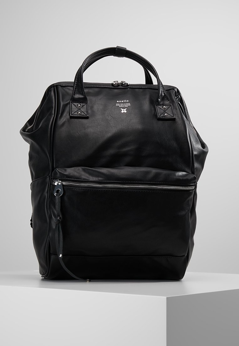Mochila de cuero negro con asas dobles, bolsillo frontal con cremallera, textura suave, detalle del logo en la parte frontal y una silueta estructurada.