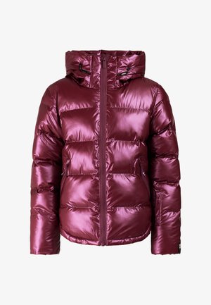 Jonge vrouw staat in een glanzend paarse pufferjas, paarse broek, zwarte handschoenen en laarzen en een roze gebreide muts.