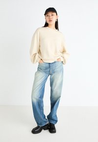 Krämmärrad sweatshirt, ljusblå vida jeans och svarta skopunkter. Slät textur, avslappnad passform och blekt denimfinish.