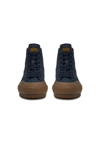 Augsti zili sporta apavi tumši zilā audumā ar brūnām gumijas zolēm. Tiem ir apaļa purngala forma, auklu aizdare un G-Star logotips uz mēles.