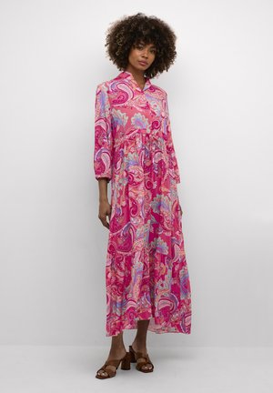 Langes, pinkes Paisleymuster-Kleid mit einem Knopfkragen und Dreiviertelärmeln. Leichter Stoff mit fließendem Schnitt. Braune Absatzsandalen.