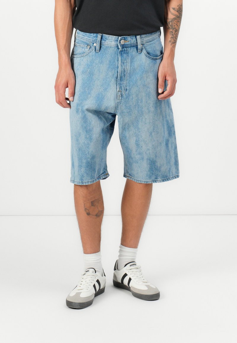 Lys blå denimshorts med avslappet passform, enkel fem-lommers design og frayed kant, parret med hvite joggesko og ankelstrømper.