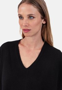 Schwarzer V-Ausschnitt-Pullover mit strukturierter Oberfläche, lockerem Schnitt und gerippten Details am Ausschnitt, ideal zum Schichten.