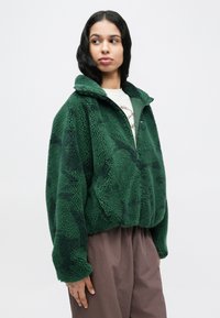 Πράσινο φλις πανωφόρι με ψηλό γιακά, διαθέτει ημιδιάφανο φερμουάρ μπροστά και υφή υφάσματος, σχεδιασμένο με άνετη εφαρμογή και υπερμεγέθη σιλουέτα.