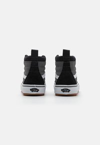 Sneaker alte con tomaia in suede nero e grigio, suola intermedia bianca e suola in gomma marrone con il logo Vans sul tallone.