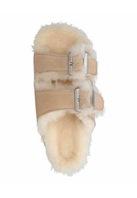 Beige instap-slipper met twee verstelbare zilveren gespen, zachte schapenvacht voering en een gestructureerde suède bovenkant. Afgeronde teennorm.