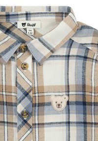 Geruite button-up shirt in beige, wit en blauw katoen. Kenmerken zijn ronde gouden knopen en een geborduurd berenpatch op de borst.