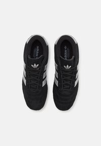 Black suede sneakers featuring three metallic silver stripes, round toe, black laces, and branded inner soles.
