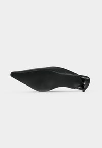 Chaussure à talon haut noire à bout pointu vue de la semelle, avec un talon fin et une semelle lisse texturée.