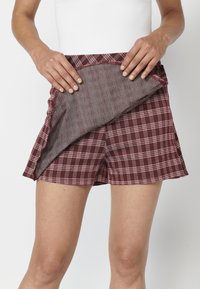 Kockás nadrág bordó és fehér színösszeállítással, amelynek a derékrésznél és az oldalon egy texturált belső bélés látható.