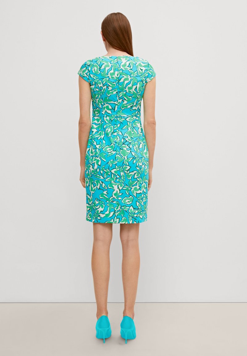 Ärmelloses, eng anliegendes Kleid in Türkis mit einem grün-weißen Blumenmuster. Glatte Textur, knielang, kombiniert mit passenden blauen Absätzen.