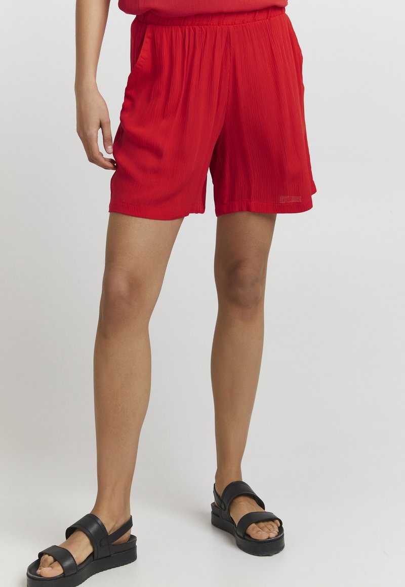Shorts plissés rouges avec une taille élastique. Tissu léger, longueur mi-cuisse et coupe décontractée. Assortis à des sandales à plateforme noires.
